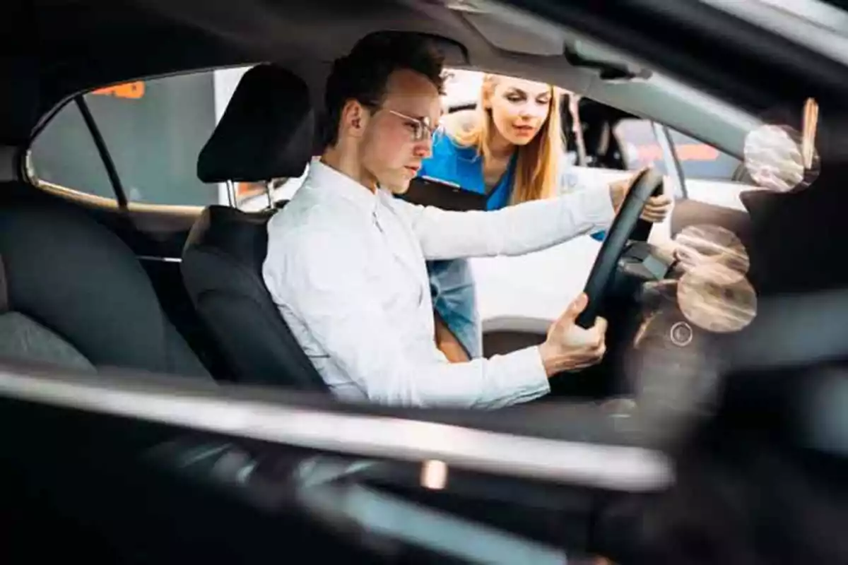 Un hombre sentado en el asiento del conductor de un automóvil mientras una mujer le muestra algo desde fuera del vehículo.