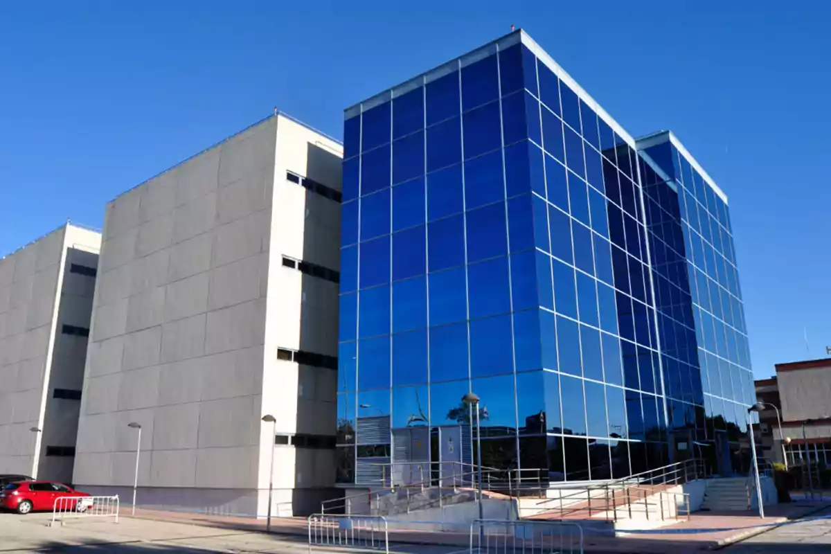 Edificio moderno con fachada de vidrio azul reflejando el cielo en un día soleado.