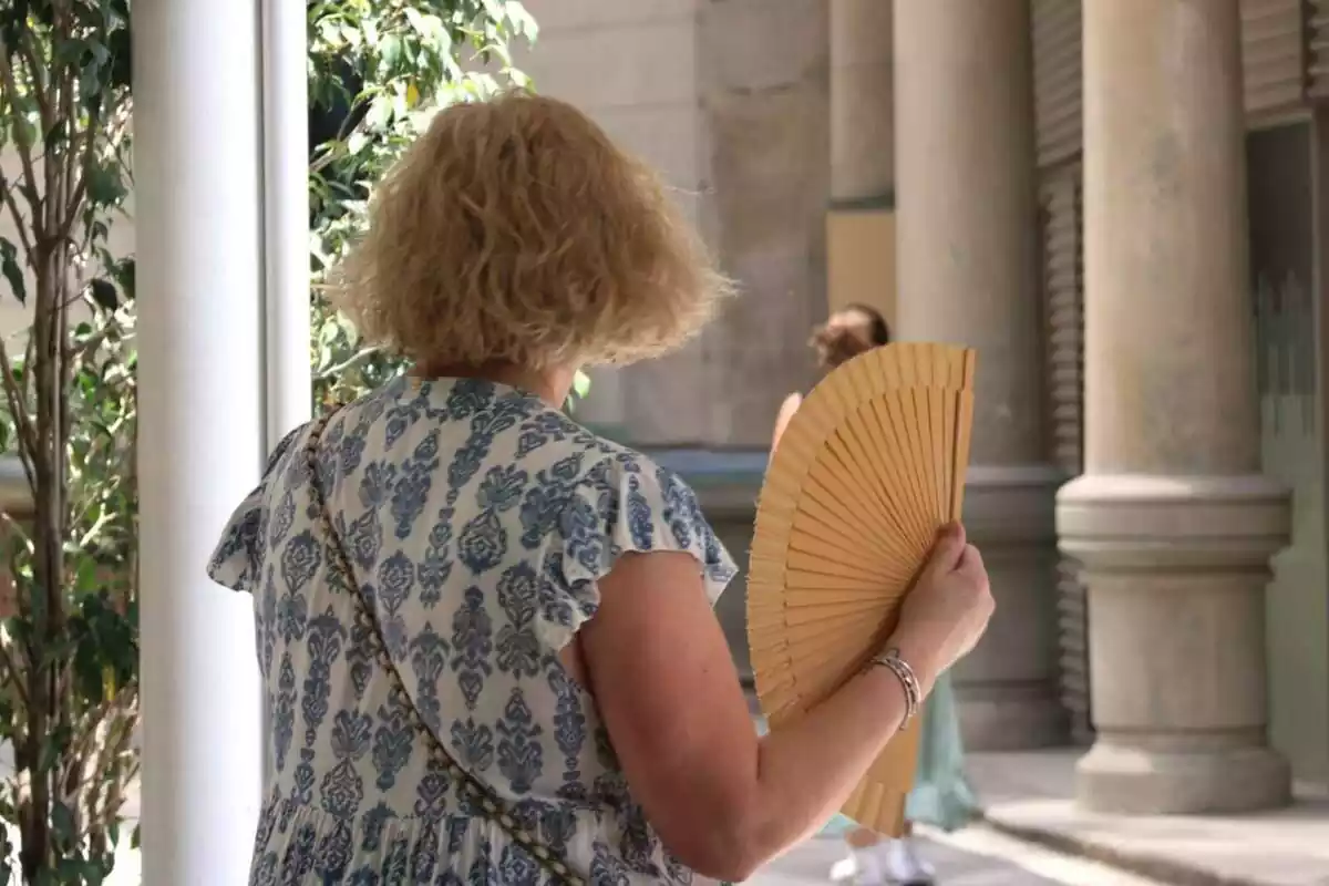 Una señora de espaldas ventándose con un abanico por el calor Una señora de espaldas ventándose con un abanico por el calor