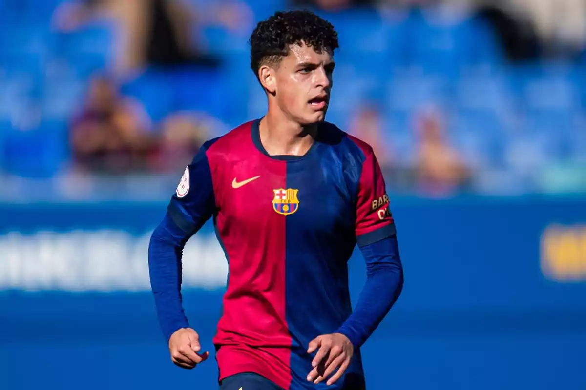 Jugador de fútbol con uniforme azul y rojo del FC Barcelona en un partido, con fondo de gradas azules desenfocadas Jugador de fútbol con uniforme azul y rojo del FC Barcelona en un partido, con fondo de gradas azules desenfocadas