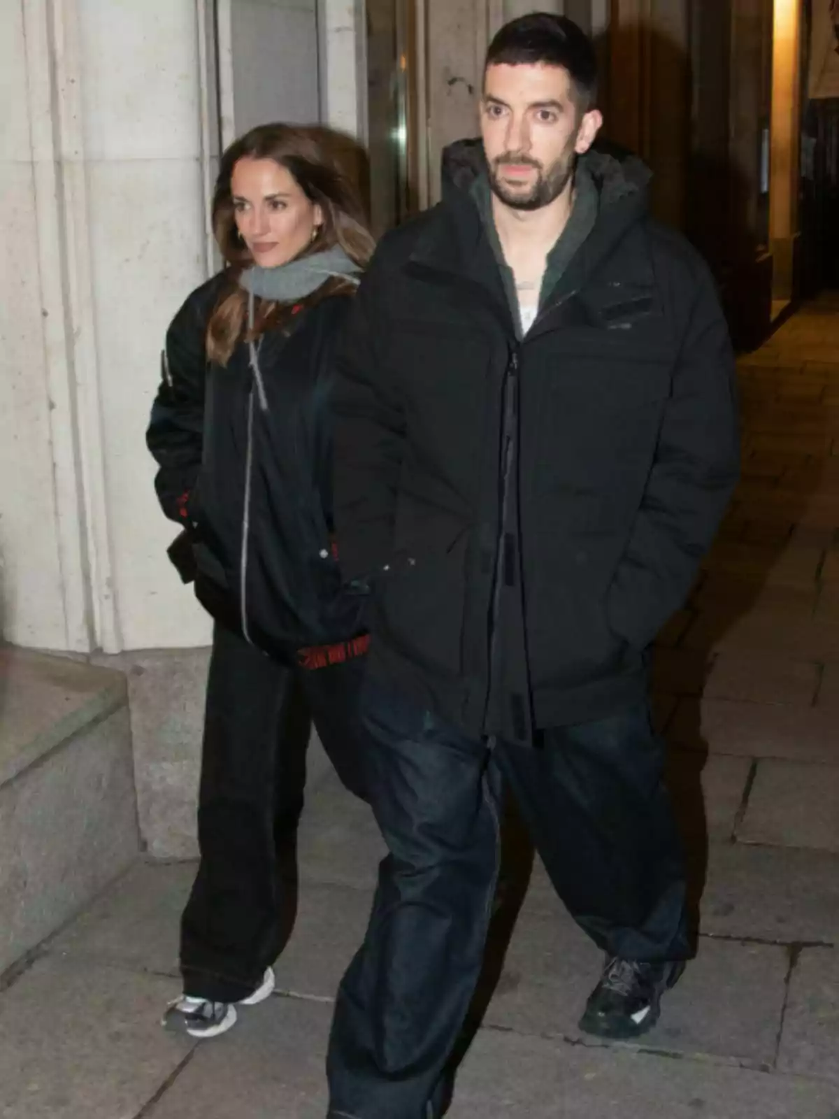 Silvia Alonso y David Broncano camina por la acera durante la noche vistiendo ropa abrigada y oscura Silvia Alonso y David Broncano camina por la acera durante la noche vistiendo ropa abrigada y oscura