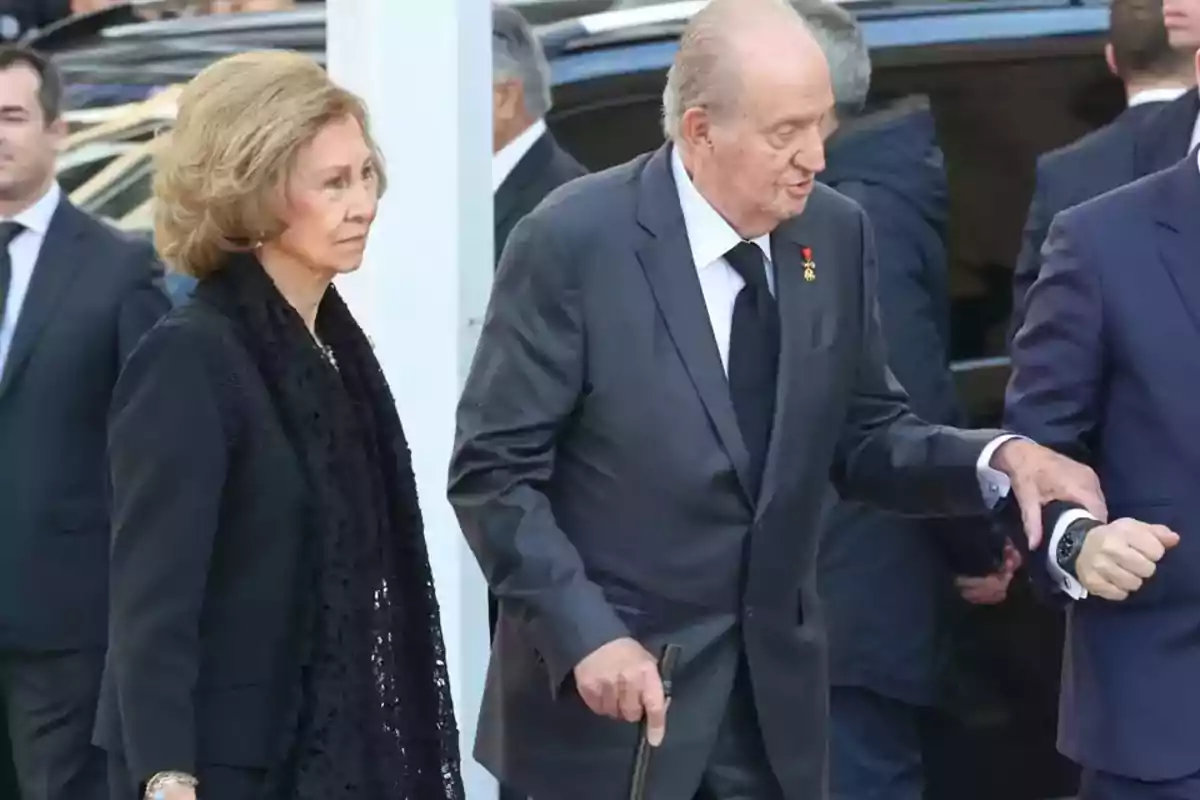 An elderly couple dressed in black walks among a group of people at a formal event. An elderly couple dressed in black walks among a group of people at a formal event.