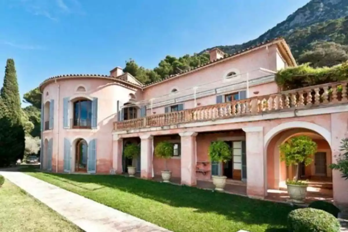 Una casa grande de color rosa con ventanas azules y un jardín bien cuidado.
