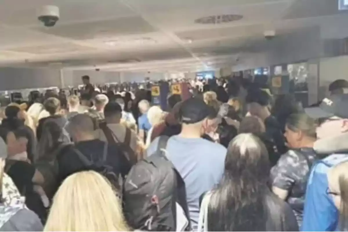 Gran cantidad de personas haciendo fila en un pasillo de aeropuerto con ambiente congestionado