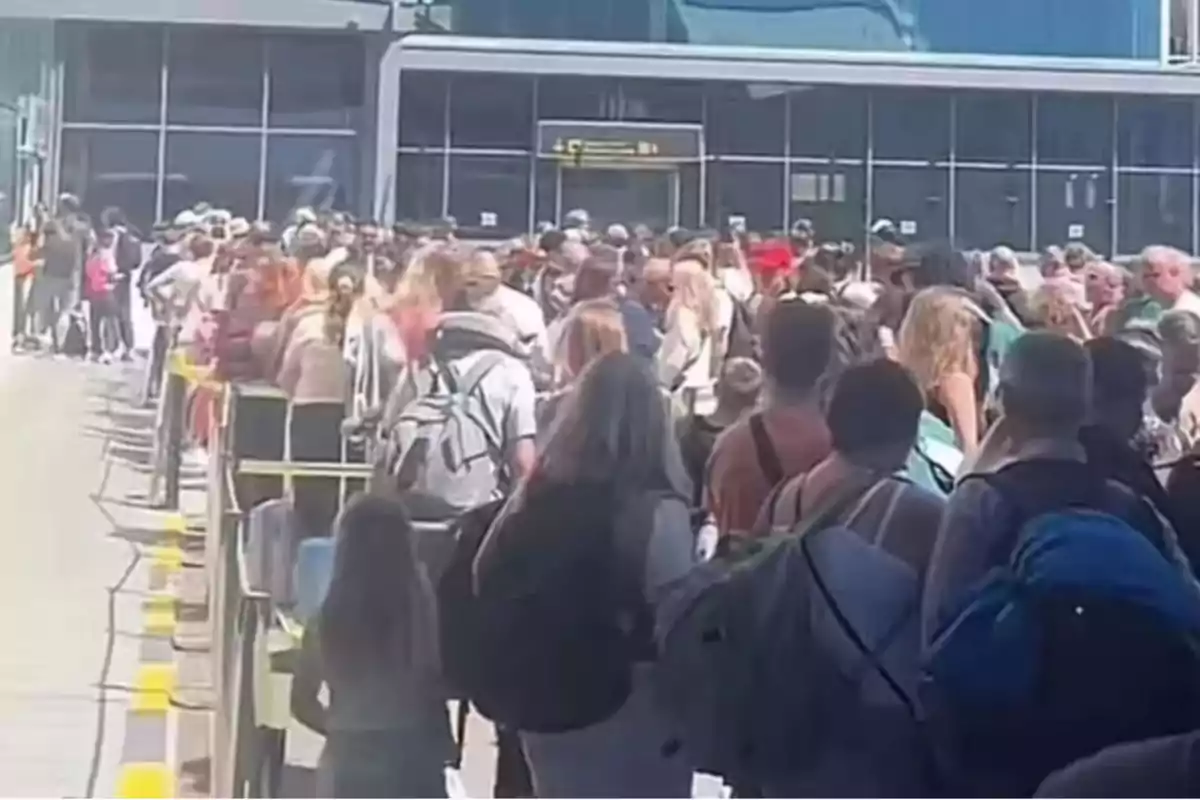 Gran cantidad de personas haciendo fila en el exterior de un edificio moderno con mochilas y maletas Gran cantidad de personas haciendo fila en el exterior de un edificio moderno con mochilas y maletas