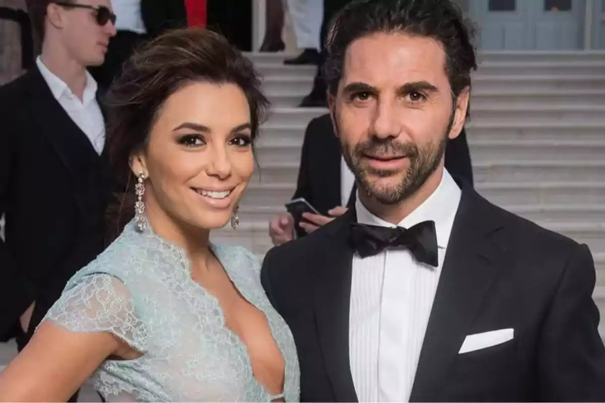 Pareja elegantemente vestida posando y sonriendo en un evento formal frente a unas escaleras Pareja elegantemente vestida posando y sonriendo en un evento formal frente a unas escaleras