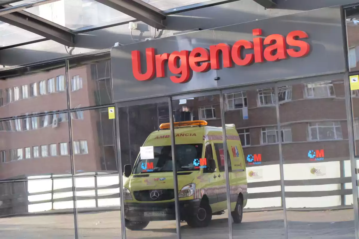 Una ambulancia está estacionada frente a la entrada de urgencias de un hospital reflejada en las ventanas del edificio.