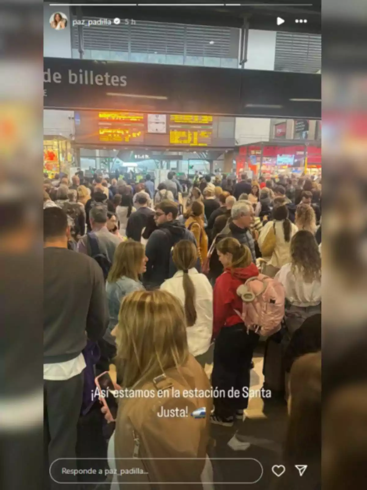Una multitud de personas se encuentra en el interior de una estación de tren, con un cartel de información de billetes visible en la parte superior. Una multitud de personas se encuentra en el interior de una estación de tren, con un cartel de información de billetes visible en la parte superior.