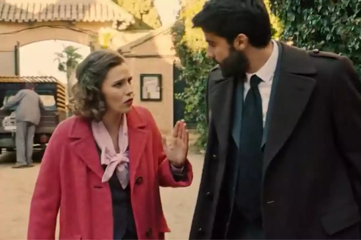 Claudia con abrigo rosa y Raúl con abrigo oscuro conversan en una calle, mientras al fondo una persona revisa la parte trasera de un vehículo antiguo. Captura de 'Sueños de libertad' Claudia con abrigo rosa y Raúl con abrigo oscuro conversan en una calle, mientras al fondo una persona revisa la parte trasera de un vehículo antiguo. Captura de 'Sueños de libertad'