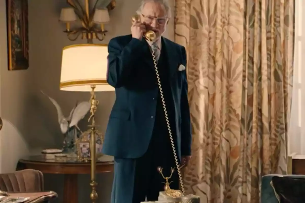 Damián de pie en una sala elegante hablando por un teléfono antiguo dorado. Captura de 'Sueños de libertad' Damián de pie en una sala elegante hablando por un teléfono antiguo dorado. Captura de 'Sueños de libertad'