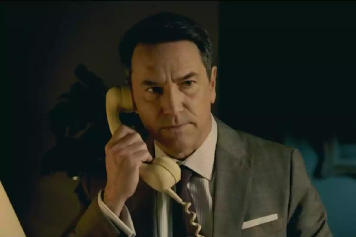 Gabriel de traje hablando por un teléfono fijo amarillo con expresión seria. Captura de 'Sueños de libertad' Gabriel de traje hablando por un teléfono fijo amarillo con expresión seria. Captura de 'Sueños de libertad'