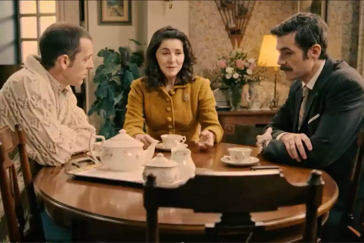 Luis, Digna y Joaquín sentadas alrededor de una mesa redonda de madera tomando té en una sala decorada con flores y una lámpara encendida al fondo. Captura de 'Sueños de libertad' Luis, Digna y Joaquín sentadas alrededor de una mesa redonda de madera tomando té en una sala decorada con flores y una lámpara encendida al fondo. Captura de 'Sueños de libertad'