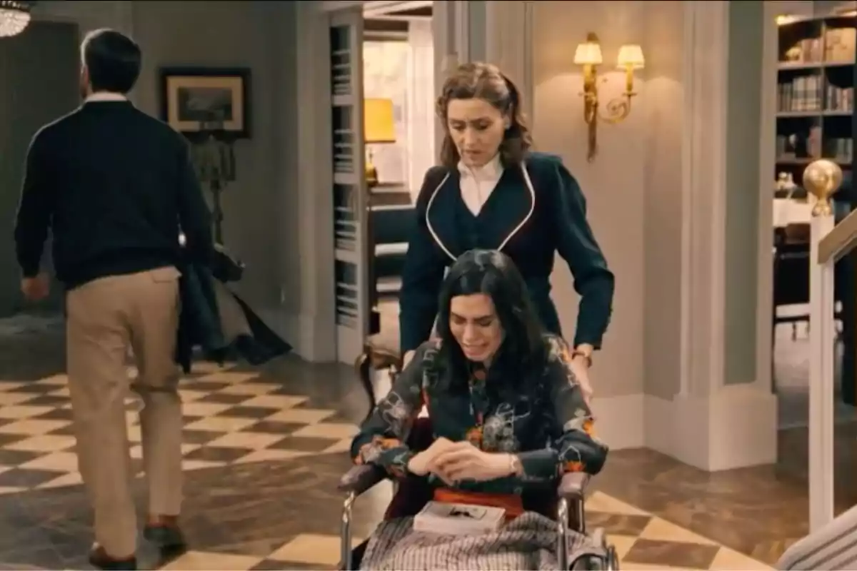 Manuela empuja una silla de ruedas en la que María está sentada y llorando mientras un hombre se aleja caminando en una elegante sala. Captura de 'Sueños de libertad' Manuela empuja una silla de ruedas en la que María está sentada y llorando mientras un hombre se aleja caminando en una elegante sala. Captura de 'Sueños de libertad'