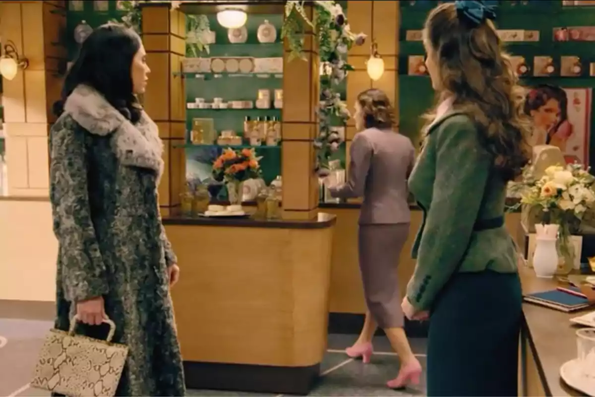Tres mujeres elegantemente vestidas se encuentran en el interior de una tienda decorada con flores y productos de belleza en estantes. Captura de 'Sueños de libertad' Tres mujeres elegantemente vestidas se encuentran en el interior de una tienda decorada con flores y productos de belleza en estantes. Captura de 'Sueños de libertad'
