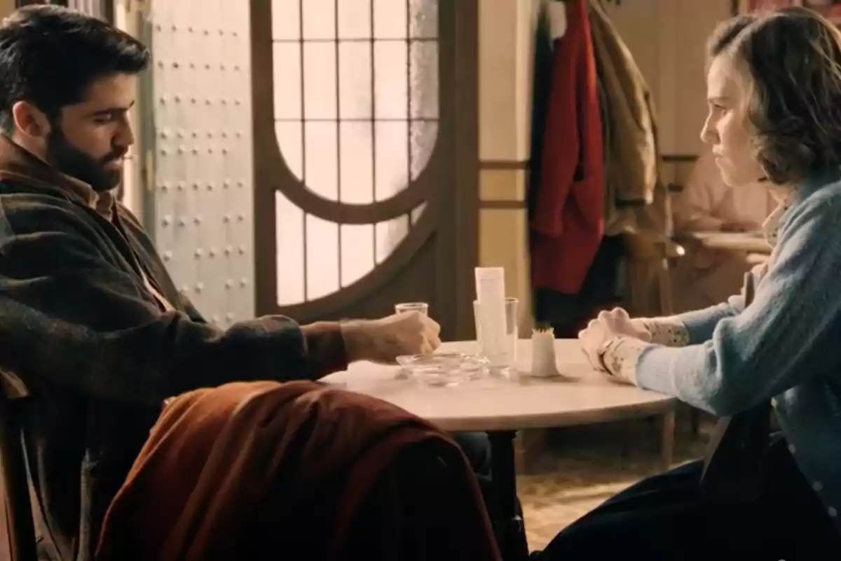 Raúl y Marta sentadas frente a frente en una mesa de café, con expresiones serias, en un ambiente interior cálido y acogedor. Captura de 'Sueños de libertad' Raúl y Marta sentadas frente a frente en una mesa de café, con expresiones serias, en un ambiente interior cálido y acogedor. Captura de 'Sueños de libertad'