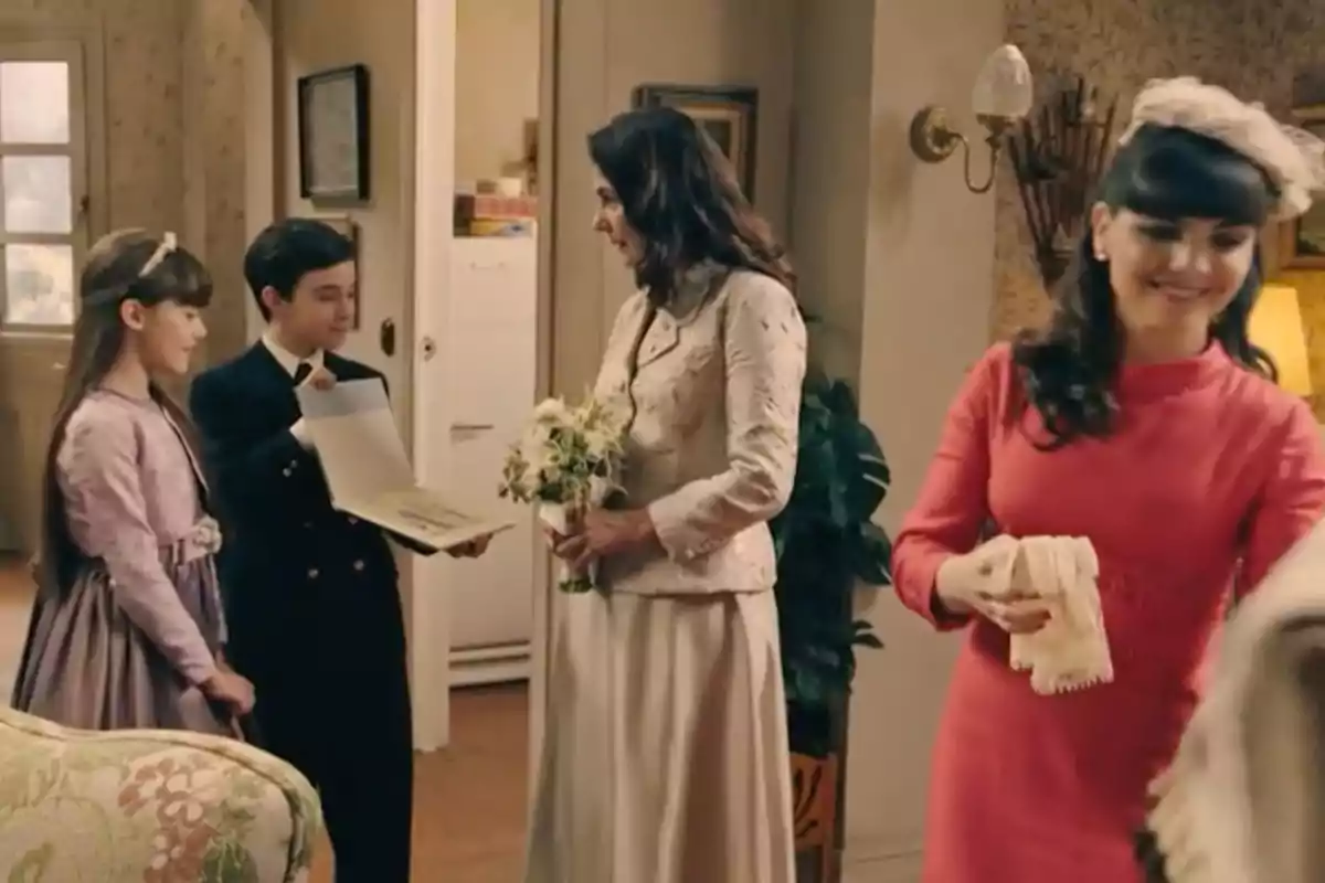 Cuatro personas elegantemente vestidas interactúan en una sala decorada de manera clásica, una mujer sostiene un ramo de flores mientras un niño le muestra un libro abierto y una niña observa sonriente, al fondo otra mujer con vestido rosa sonríe mientras sostiene unos guantes. Captura de 'Sueños de libertad' Cuatro personas elegantemente vestidas interactúan en una sala decorada de manera clásica, una mujer sostiene un ramo de flores mientras un niño le muestra un libro abierto y una niña observa sonriente, al fondo otra mujer con vestido rosa sonríe mientras sostiene unos guantes. Captura de 'Sueños de libertad'