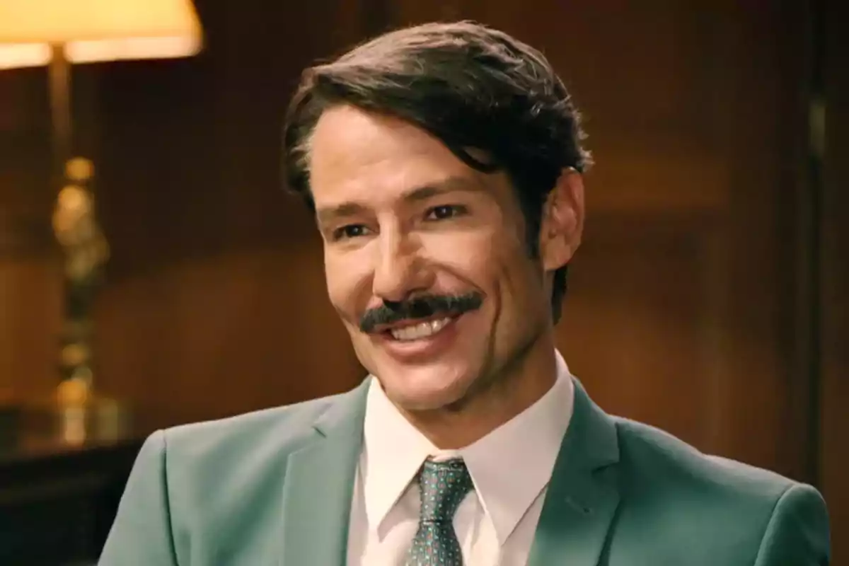 Pelayo con bigote sonríe mientras lleva un traje verde y corbata en un ambiente interior iluminado. Captura de 'sueños de libertad' Pelayo con bigote sonríe mientras lleva un traje verde y corbata en un ambiente interior iluminado. Captura de 'sueños de libertad'