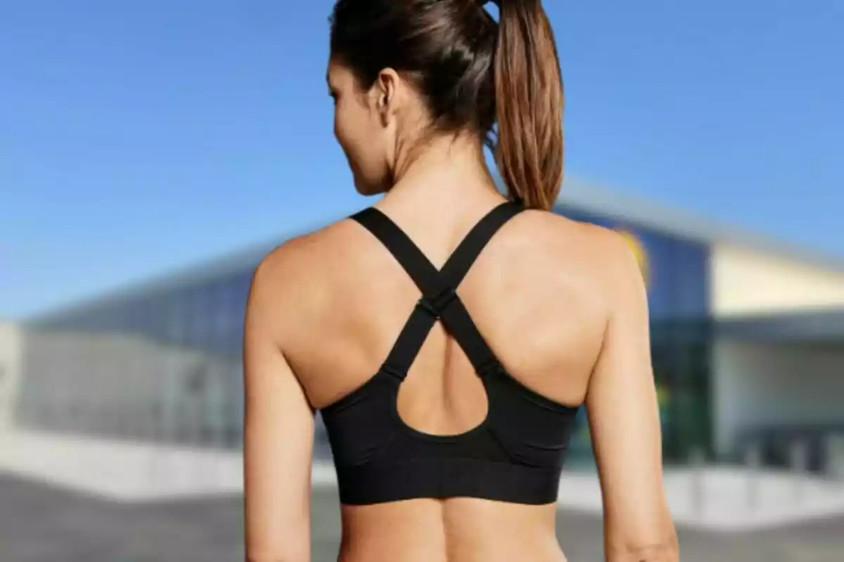 Mujer de espaldas con top deportivo negro y cabello recogido en una cola de caballo frente a un edificio moderno. Mujer de espaldas con top deportivo negro y cabello recogido en una cola de caballo frente a un edificio moderno.