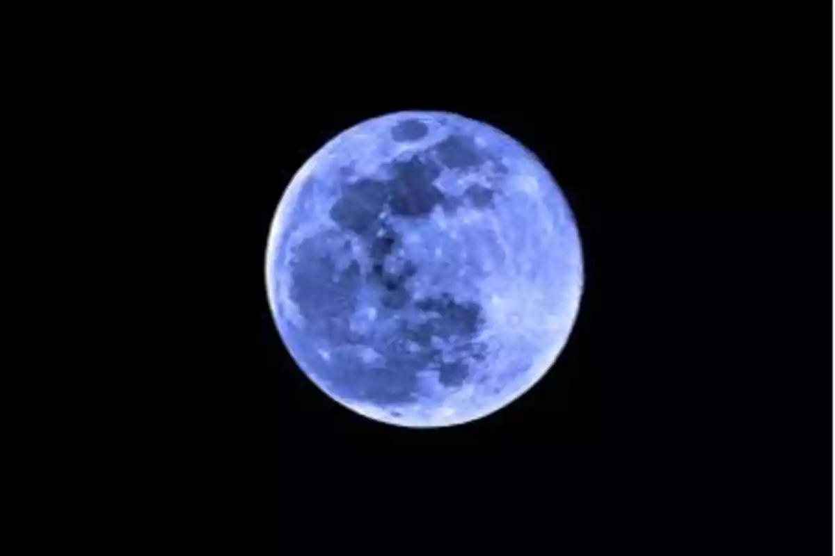 Imagen de la luna llena con un tono azulada sobre un fondo negro.