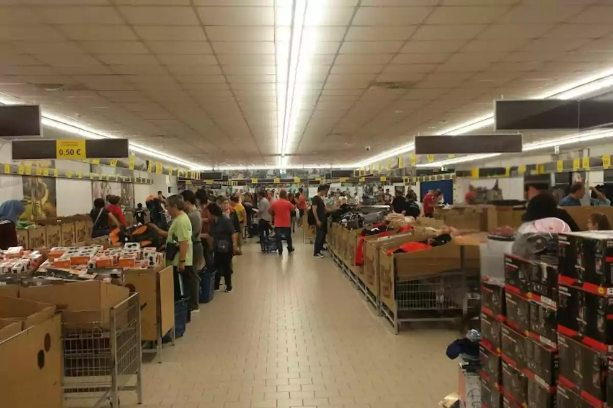 Personas comprando en un supermercado con pasillos llenos de productos y cajas de cartón. Personas comprando en un supermercado con pasillos llenos de productos y cajas de cartón.