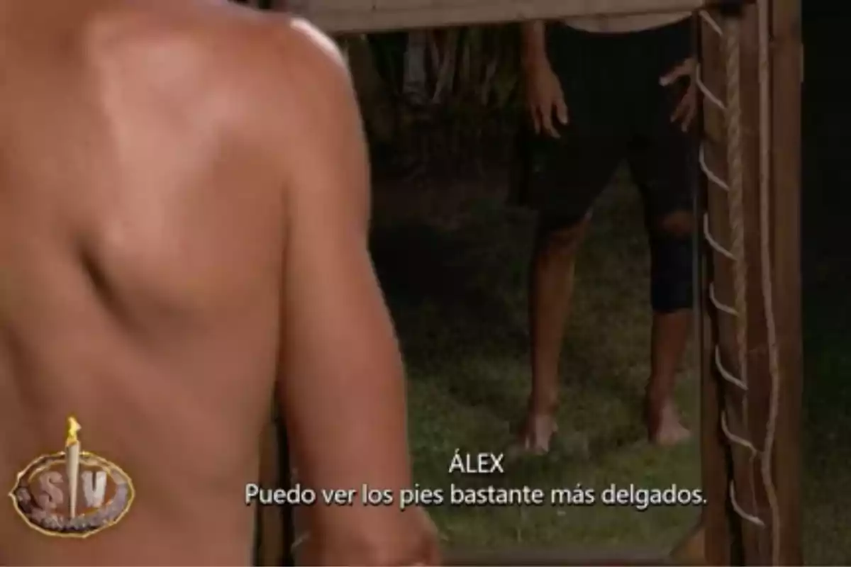 Álex Adrover sin camiseta se observa en un espejo de cuerpo entero al aire libre mientras en la pantalla aparecen subtítulos que dicen Álex Adrover sin camiseta se observa en un espejo de cuerpo entero al aire libre mientras en la pantalla aparecen subtítulos que dicen