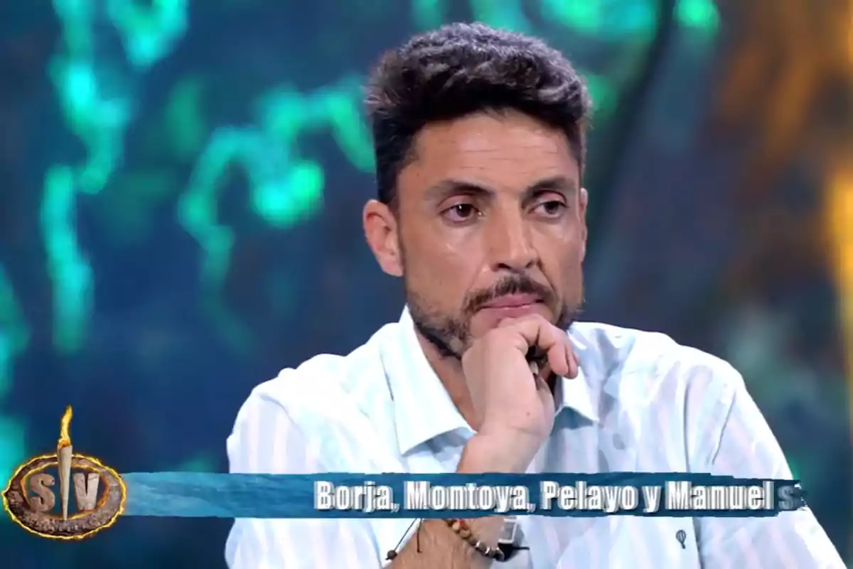 Carlos Calderón con camisa blanca aparece pensativo en un programa de televisión, con un fondo desenfocado en tonos verdes y azules. Captura de 'Supervivientes' Carlos Calderón con camisa blanca aparece pensativo en un programa de televisión, con un fondo desenfocado en tonos verdes y azules. Captura de 'Supervivientes'