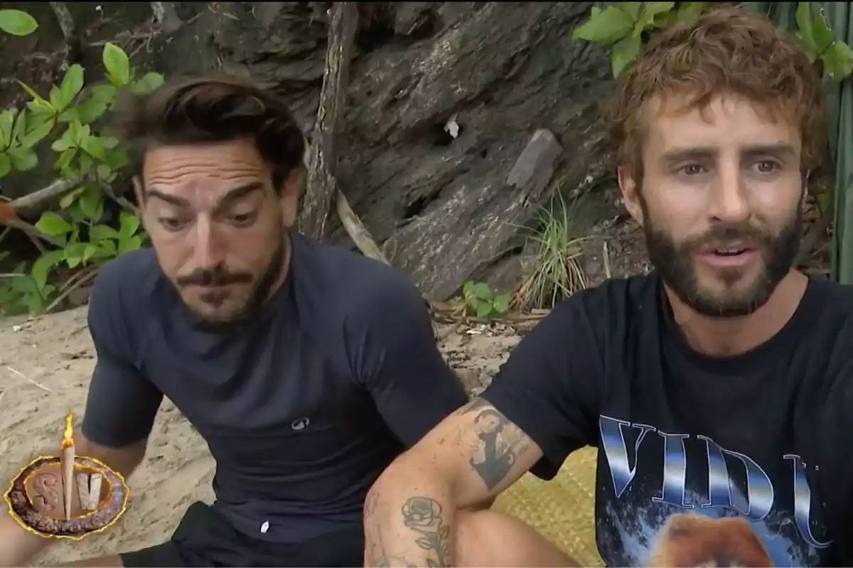 Damián Quintero y Pelayo Díaz sentados en una playa, rodeados de vegetación, uno de ellos lleva una camiseta negra con un diseño gráfico. Captura de 'Supervivientes' Damián Quintero y Pelayo Díaz sentados en una playa, rodeados de vegetación, uno de ellos lleva una camiseta negra con un diseño gráfico. Captura de 'Supervivientes'