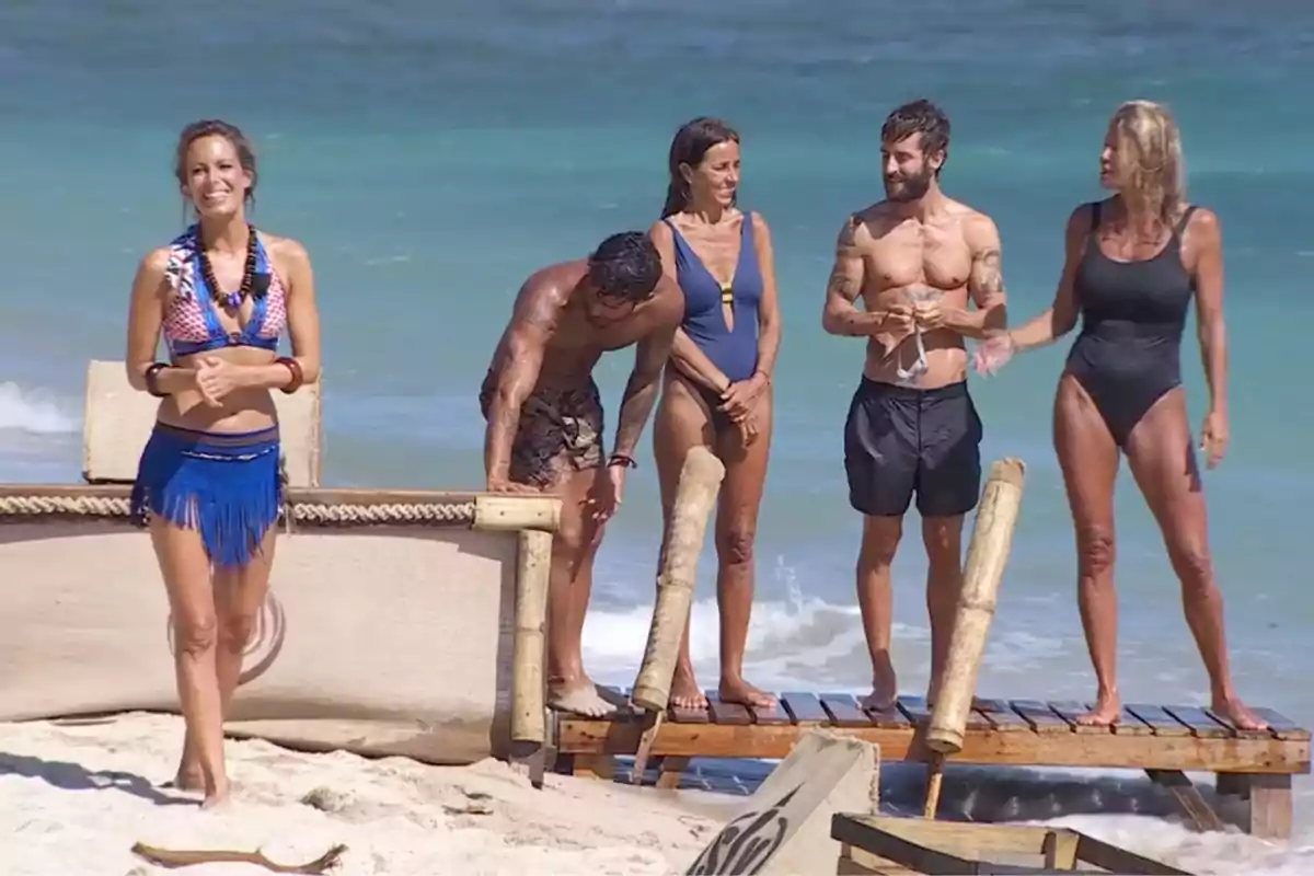 Un grupo de personas en trajes de baño está de pie en una playa junto al mar, con una mujer al frente sonriendo. Captura de 'Supervivienes' Un grupo de personas en trajes de baño está de pie en una playa junto al mar, con una mujer al frente sonriendo. Captura de 'Supervivienes'