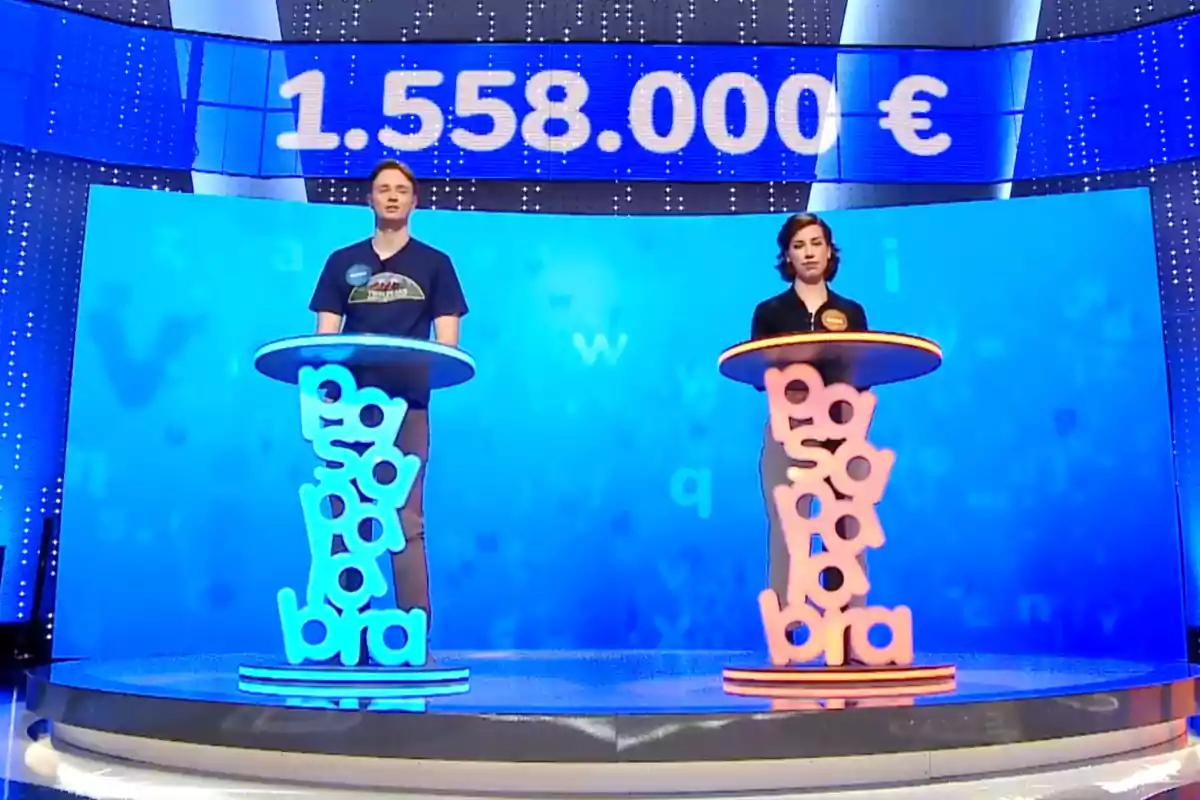 Manu y Rosa están de pie en un plató de televisión con un fondo azul, cada uno detrás de un podio decorado con letras, y en la parte superior se muestra un marcador con una cantidad en euros. Captura de 'Pasapalabra' Manu y Rosa están de pie en un plató de televisión con un fondo azul, cada uno detrás de un podio decorado con letras, y en la parte superior se muestra un marcador con una cantidad en euros. Captura de 'Pasapalabra'