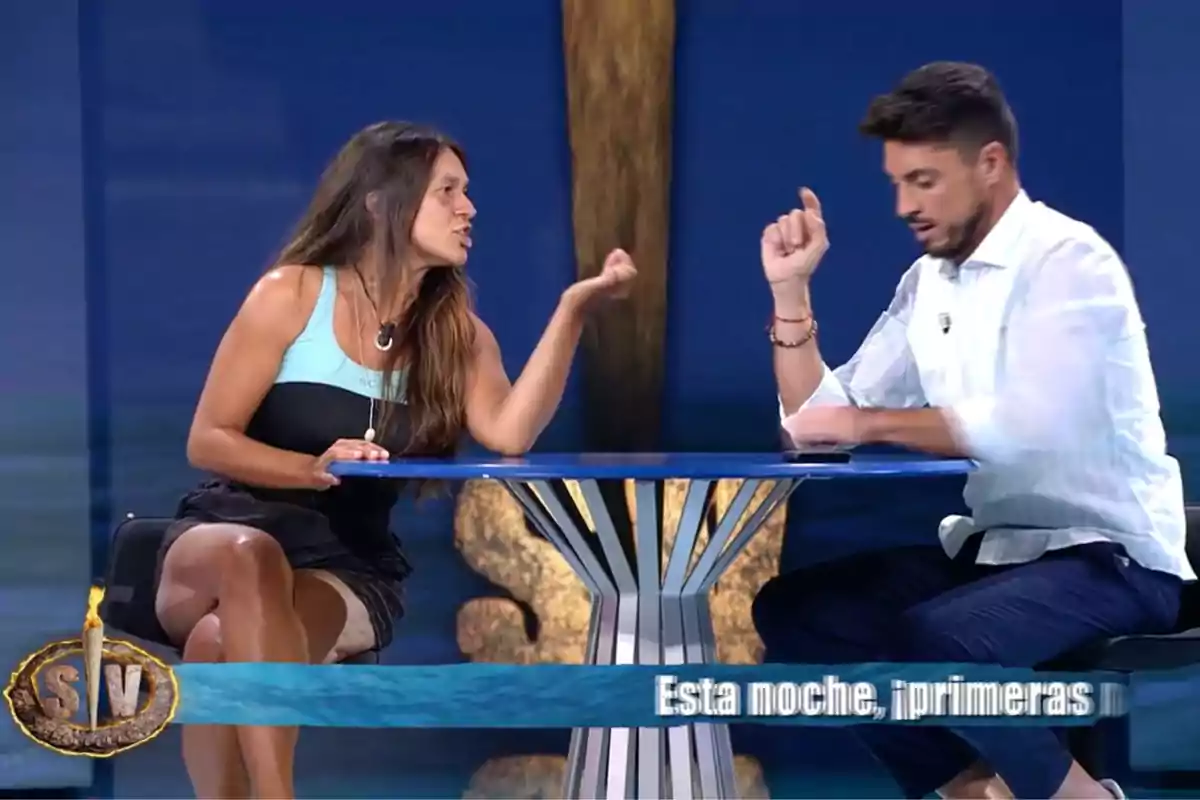 Laura Cuevas y Carlos Calderón sentadas en una mesa azul discuten gesticulando intensamente en un set de televisión con un fondo azul y un logotipo en la esquina inferior izquierda. Captura de 'Supervivientes' Laura Cuevas y Carlos Calderón sentadas en una mesa azul discuten gesticulando intensamente en un set de televisión con un fondo azul y un logotipo en la esquina inferior izquierda. Captura de 'Supervivientes'