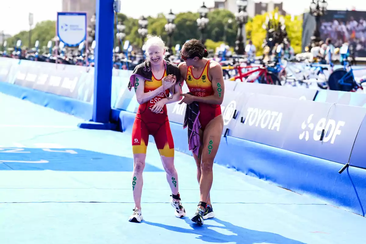 Dos atletas con uniformes de España se abrazan y sonríen en la línea de meta de una competencia de triatlón.