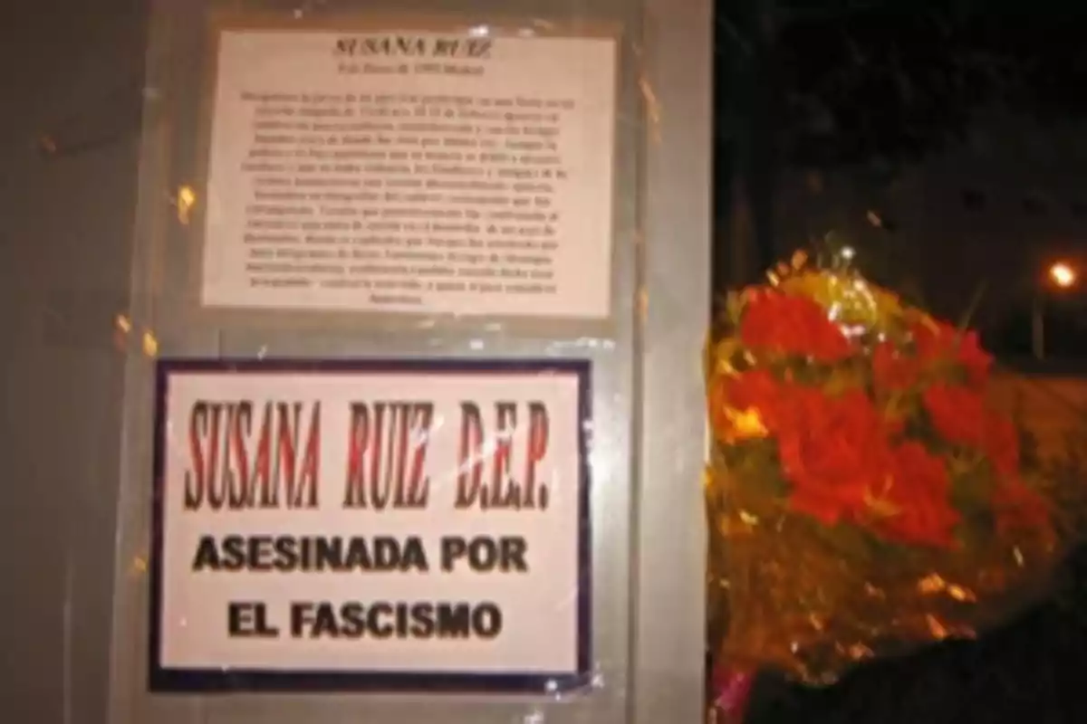 Una placa conmemorativa en memoria de Susana Ruiz, acompañada de un ramo de flores rojas.