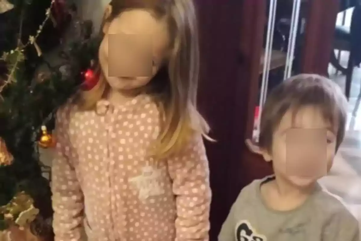 Dos niños pequeños posan junto a un árbol de Navidad decorado.