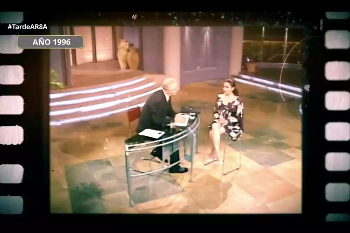 Una entrevista en un programa de televisión en el año 1996 con Xavier Sardà y Isabel Pantoja sentados en un set decorado con columnas y escaleras iluminadas. Captura de 'TardeAR' el 8 de agosto de 2024