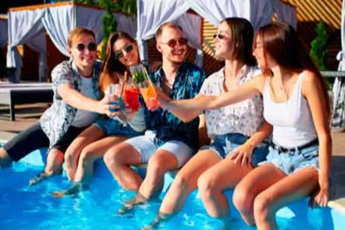 Un grupo de amigos disfrutando de bebidas junto a una piscina.
