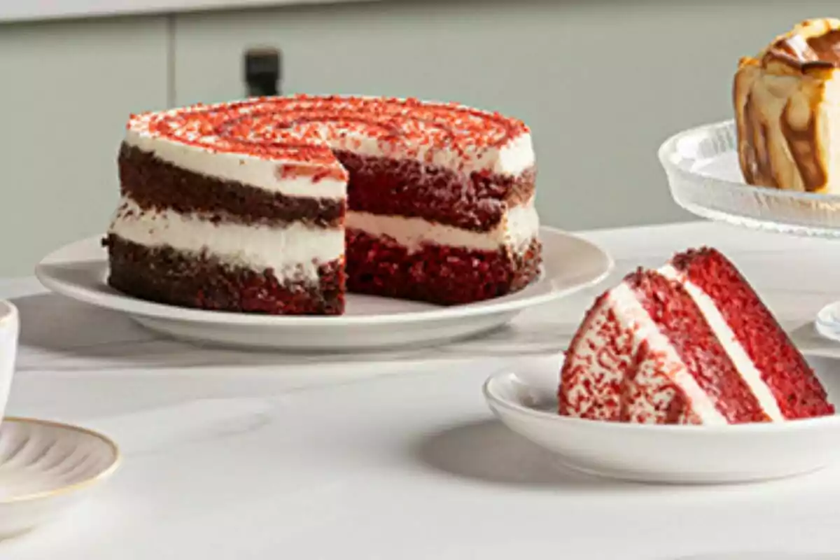 Un pastel de terciopelo rojo con capas de crema blanca servido en un plato blanco y una rebanada en un plato pequeño. Un pastel de terciopelo rojo con capas de crema blanca servido en un plato blanco y una rebanada en un plato pequeño.