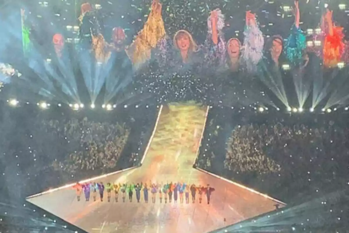 Un grupo de personas en el escenario de un concierto con luces brillantes y una gran pantalla mostrando a los artistas.