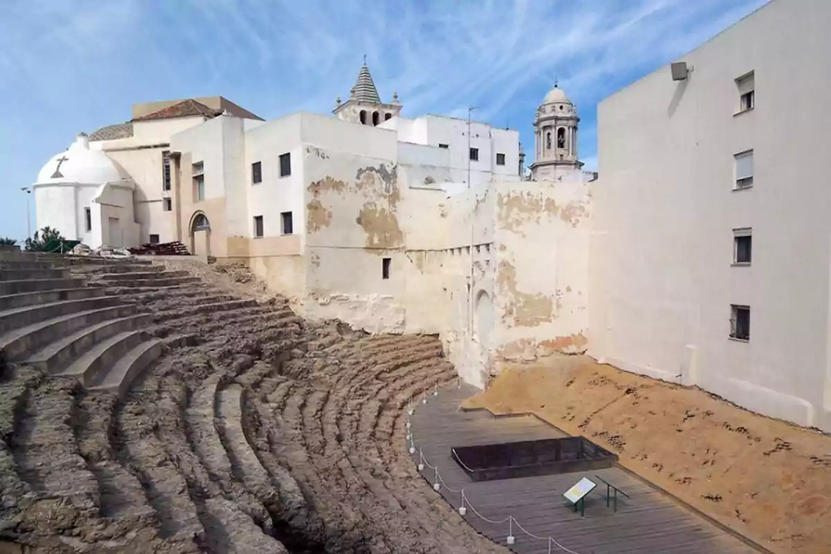 Ruinas de un antiguo teatro romano junto a edificios modernos bajo un cielo azul.