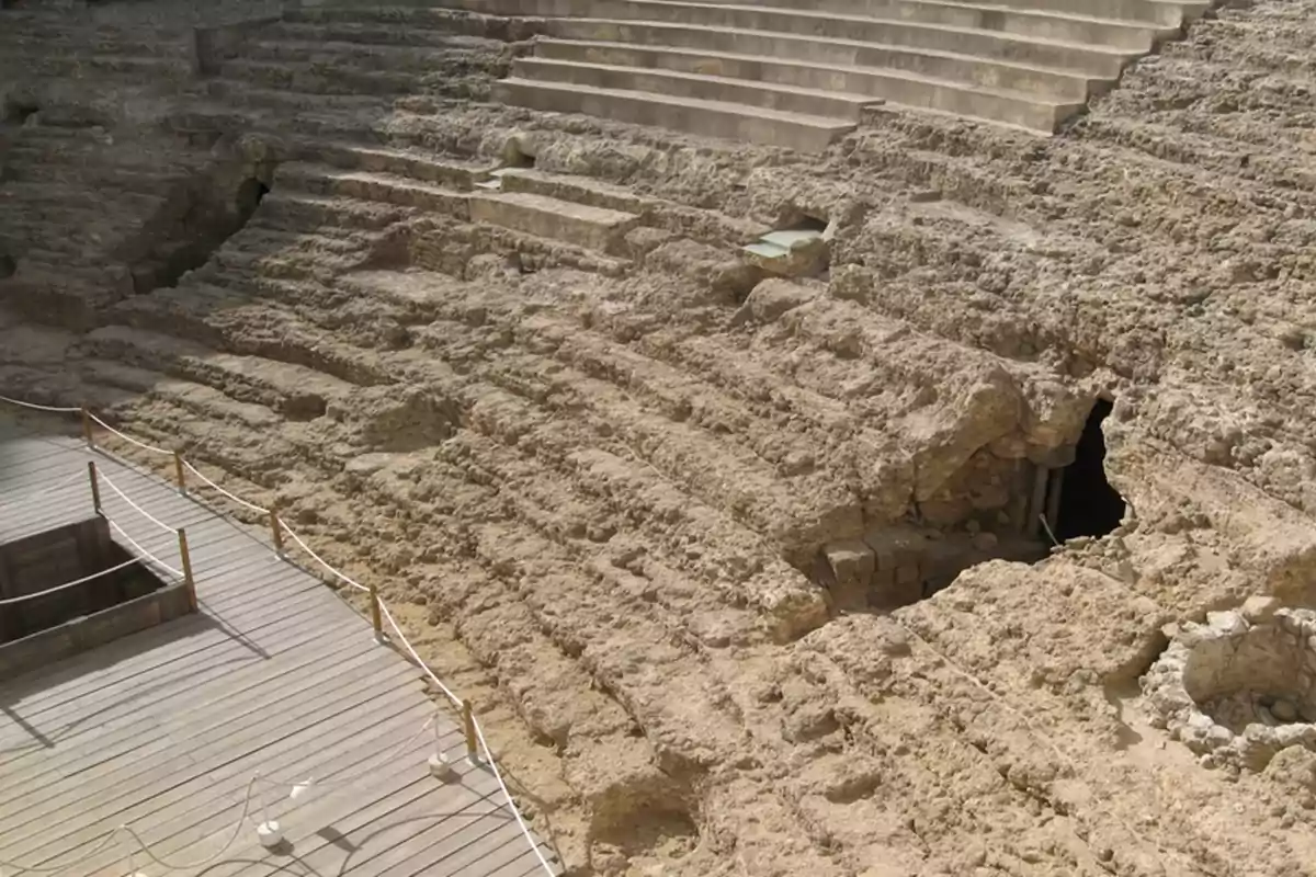 Ruinas de un antiguo teatro romano con gradas de piedra erosionadas y una plataforma de madera en primer plano.