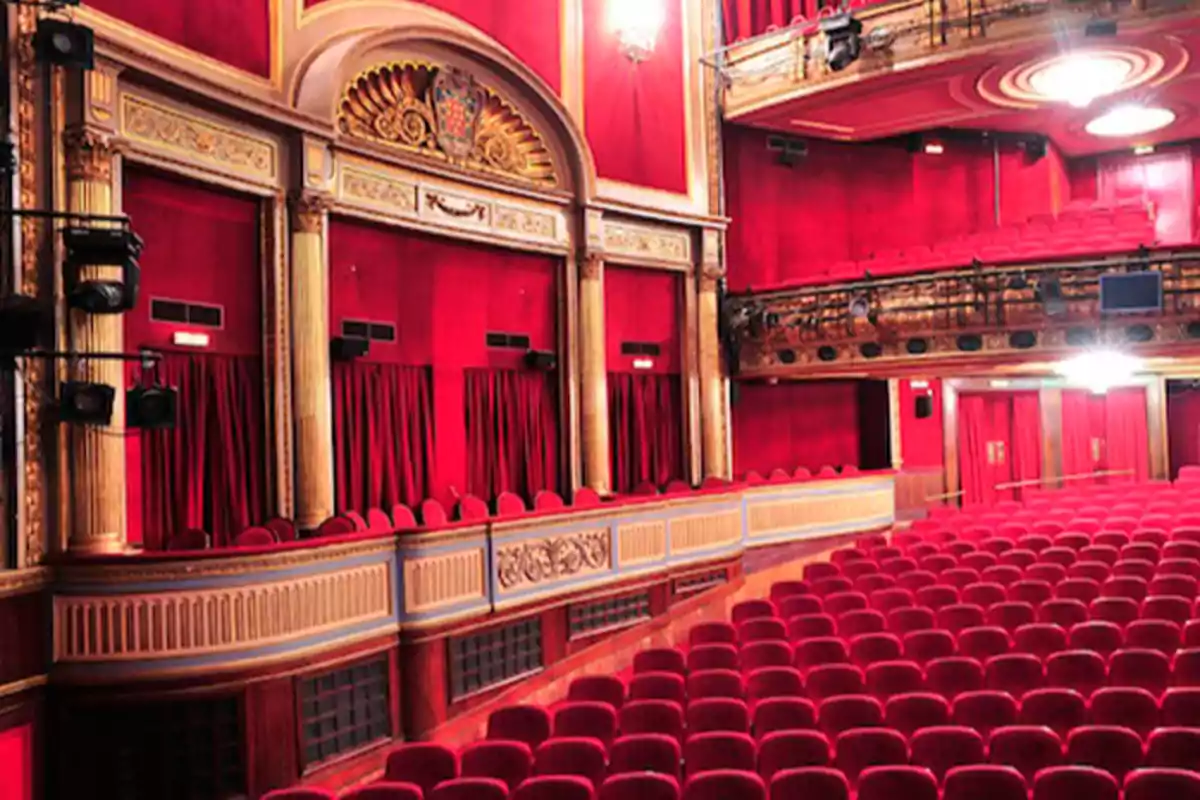 Interior de un teatro con asientos rojos y decoración dorada.