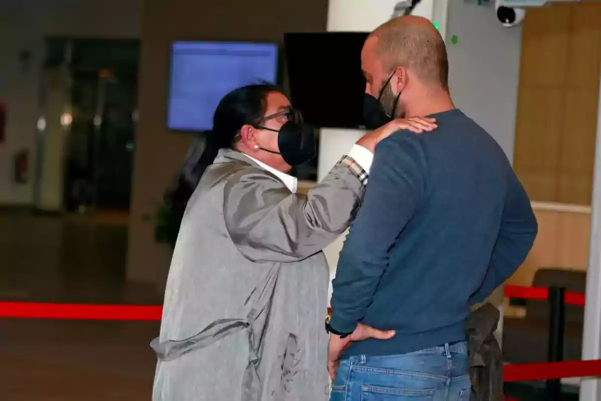 Dos personas con mascarillas conversan en un espacio interior.