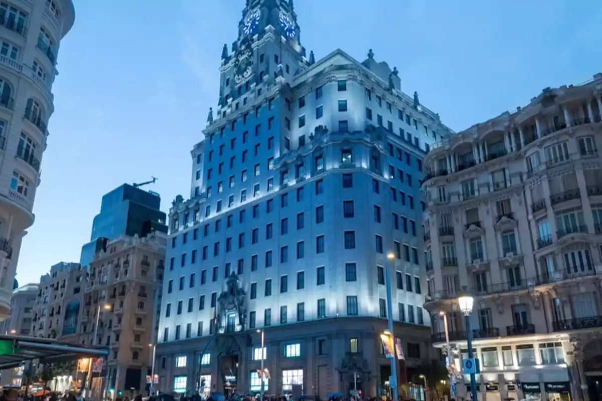 Edificio iluminado al anochecer en una calle concurrida con arquitectura clásica y moderna.