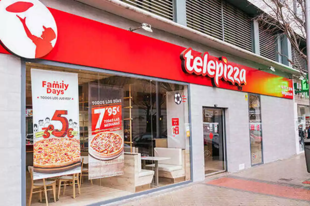 Fachada de una pizzería Telepizza con carteles promocionales en la ventana.