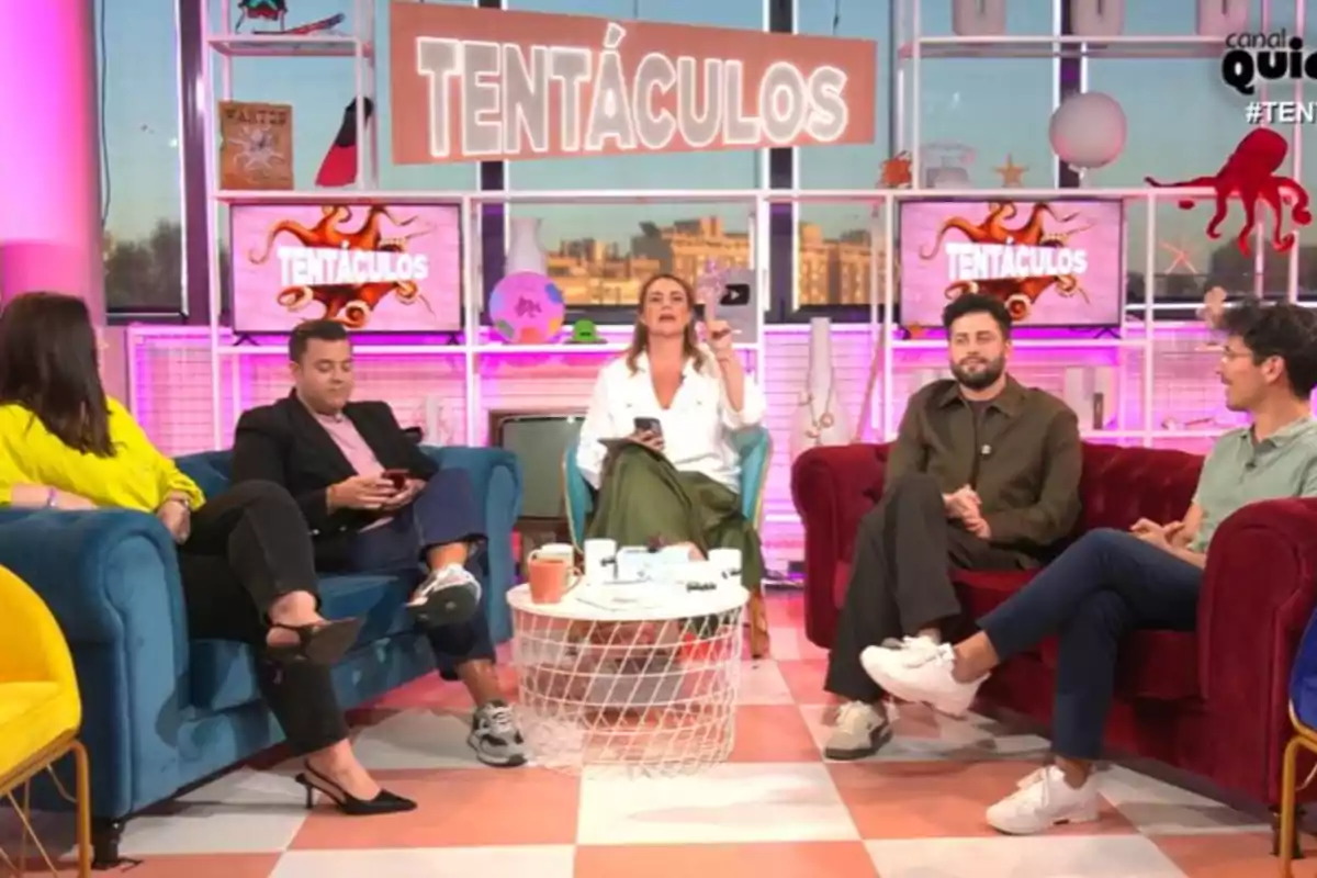 Un grupo de personas está sentado en un set de televisión colorido con el letrero Un grupo de personas está sentado en un set de televisión colorido con el letrero