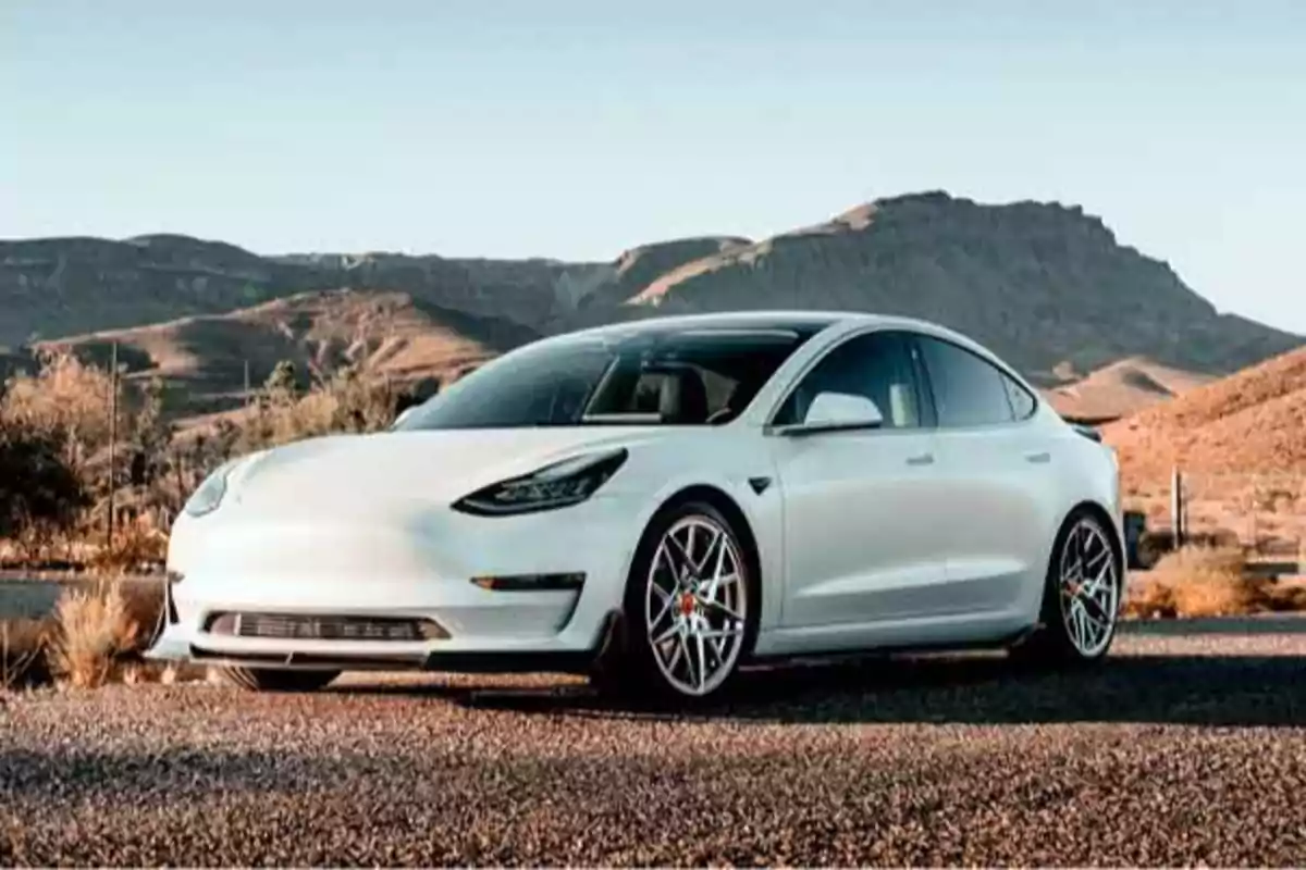 Coche eléctrico blanco estacionado en un paisaje desértico con montañas al fondo.