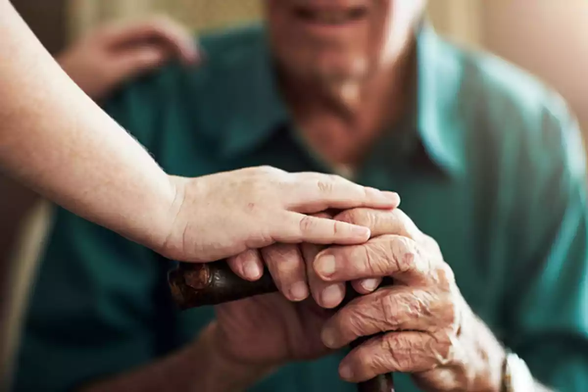 Una mano joven sostiene la mano de una persona mayor que usa un bastón.