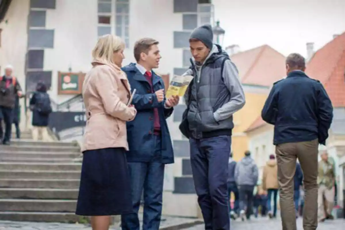 Tres personas conversando en una calle concurrida con edificios de fondo.