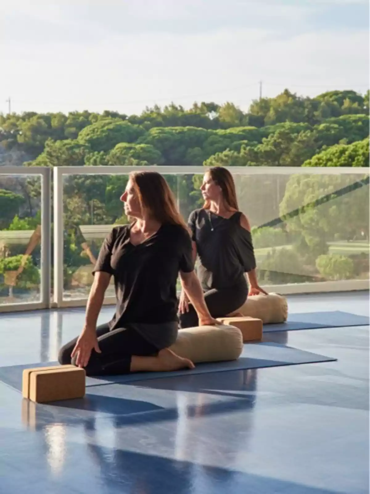 Dos mujeres practicando yoga en una terraza con vista a un paisaje verde.