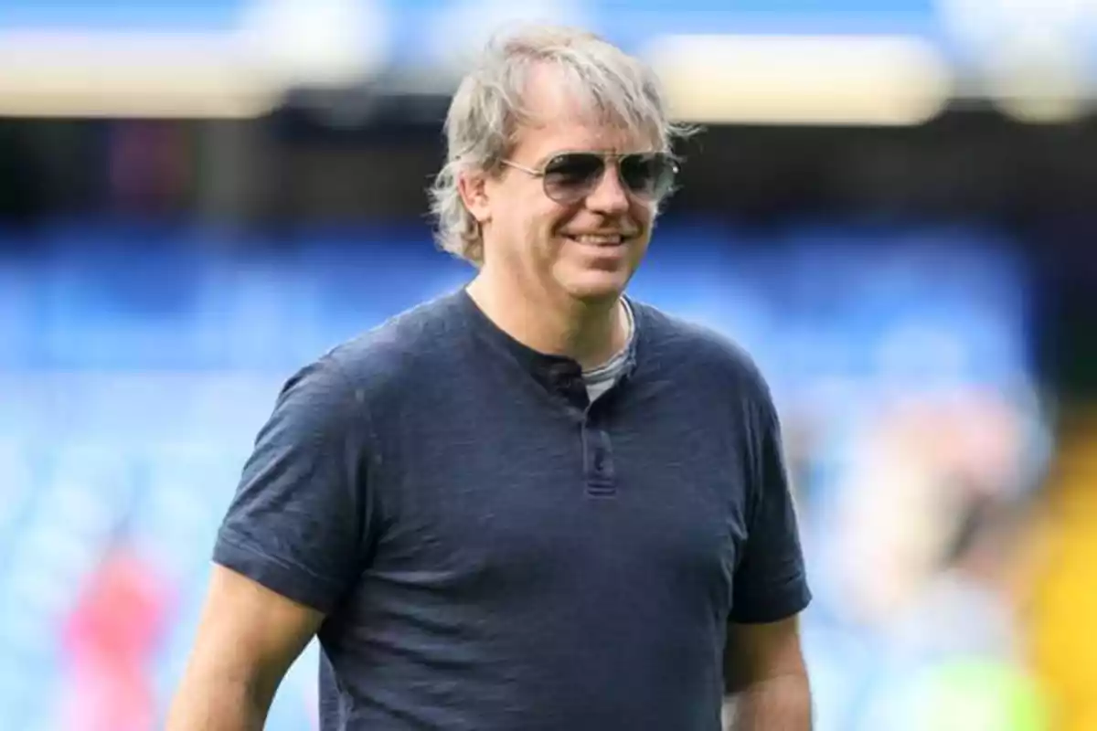 Hombre con gafas de sol y camiseta gris sonriendo en un estadio. Hombre con gafas de sol y camiseta gris sonriendo en un estadio.