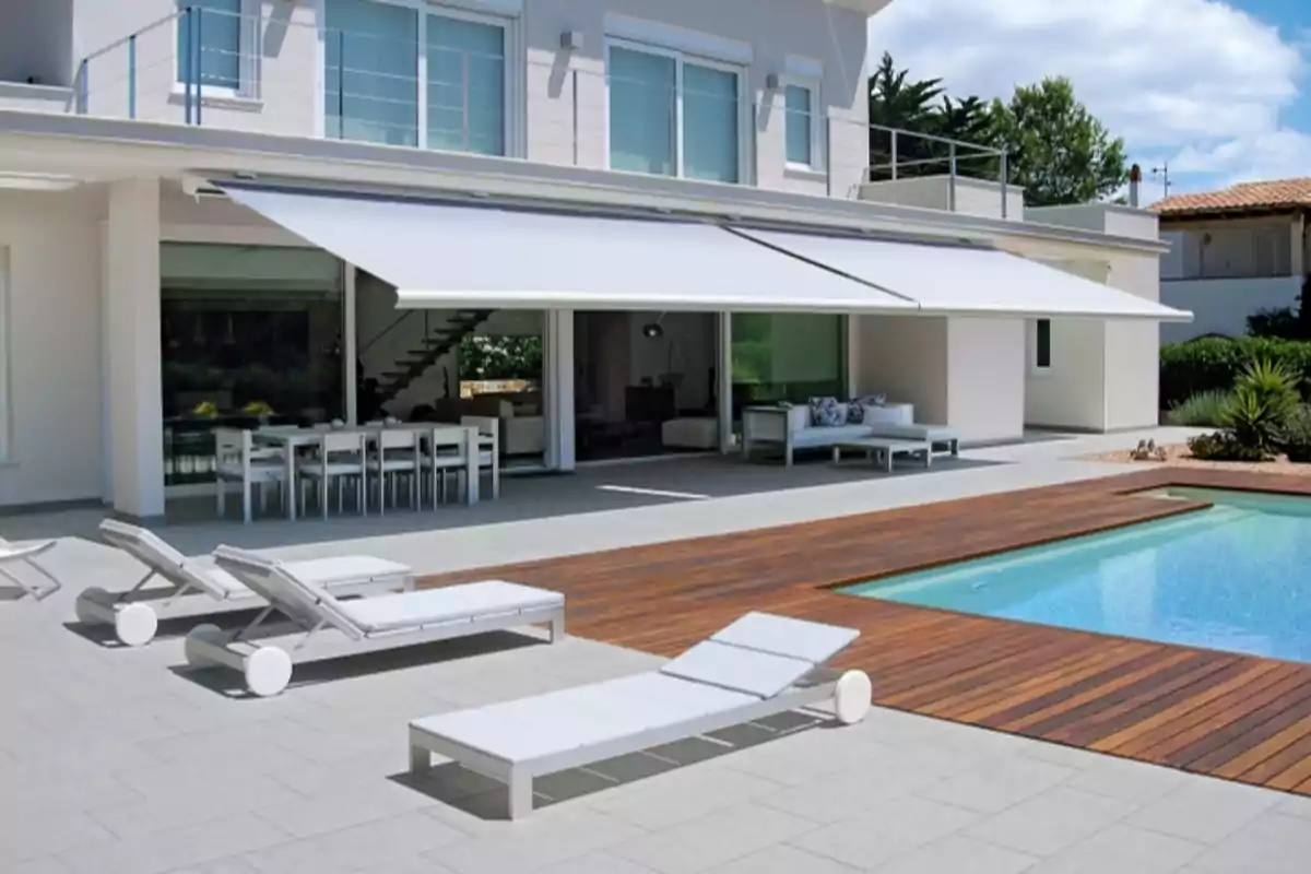 Casa moderna con piscina, tumbonas y terraza con toldo.